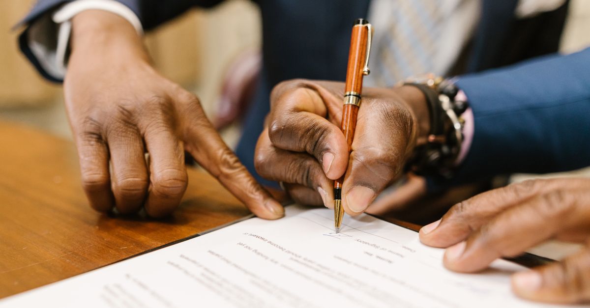Close-up of business professionals signing a legal contract in an office setting.